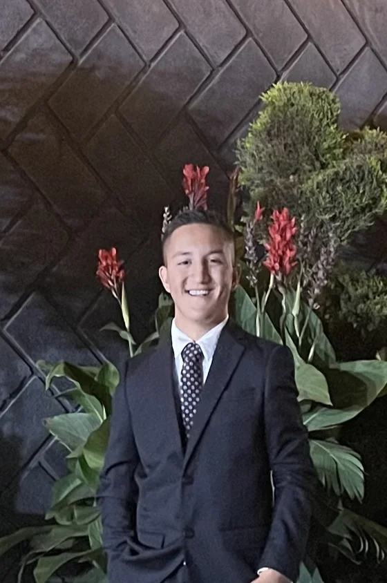 David Alvarado Correa, de traje oscuro, frente a un muro de piedra con plantas.